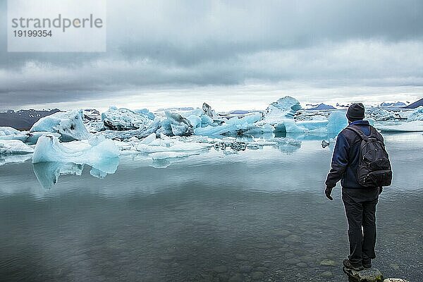 Ein junger Mann mit einem Rucksack schaut auf den Jokulsarlon Eissee im Goldenen Kreis im Süden Islands