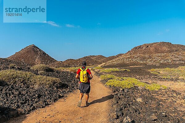 Ein junger Mann mit einem gelben Rucksack auf dem Weg nach Norden zur Isla de Lobos an der Nordküste der Insel Fuerteventura  Kanarische Inseln. Spanien