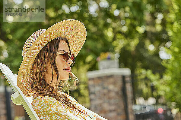 Frau mit Strohhut und Sonnenbrille entspannt im Park