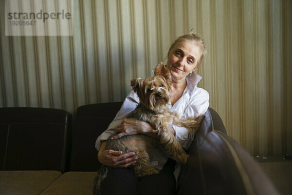 Porträt einer Frau  die einen Yorkshire-Terrier im Wohnzimmer hält