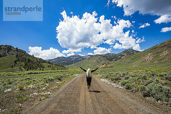 USA  Idaho  Sun Valley  Rückansicht einer älteren Frau  die mit erhobenen Armen auf der Straße steht und auf die Berge blickt