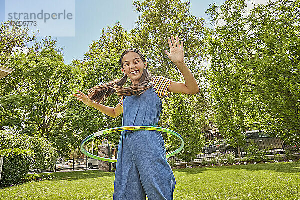 Lächelndes Mädchen (12–13) spielt mit Hula Hoop im Park