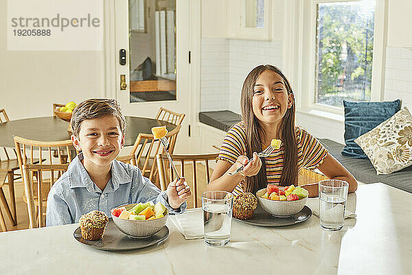 Lächelnder Junge (8-9) und Mädchen (12-13) genießen das Frühstück in der Küche