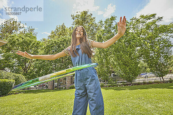 Lächelndes Mädchen (12–13) spielt mit Hula Hoop im Park