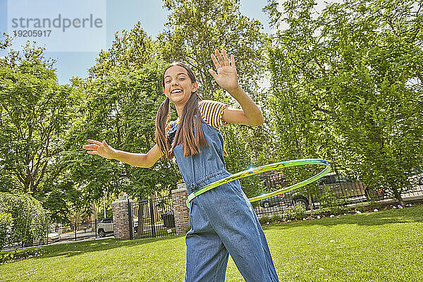 Lächelndes Mädchen (12–13) spielt mit Hula Hoop im Park