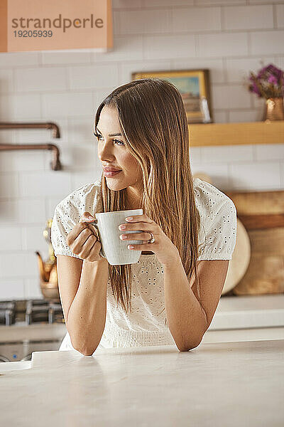 Lächelnde Frau hält Tasse in der Küche