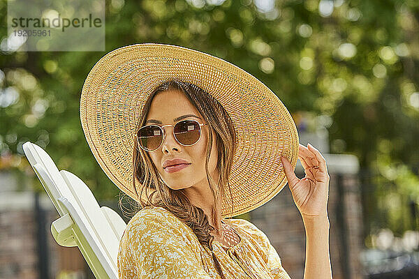 Frau mit Strohhut und Sonnenbrille entspannt im Park