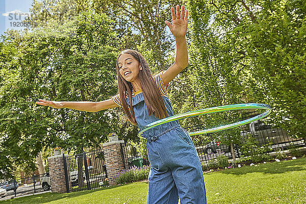 Lächelndes Mädchen (12–13) spielt mit Hula Hoop im Park