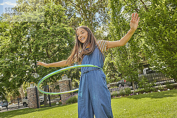 Lächelndes Mädchen (12–13) spielt mit Hula Hoop im Park