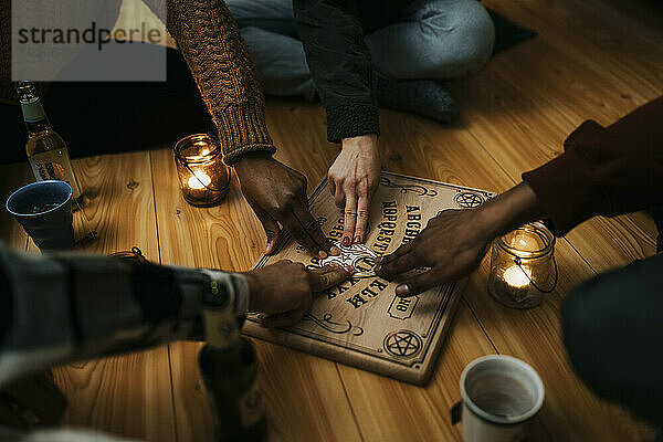 Gemischtrassige männliche und weibliche Freunde nutzen das Ouija-Brett im Haus