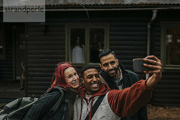 Fröhliche  gemischtrassige Freunde  die ein Selfie mit dem Smartphone machen  während im Hintergrund ein Geist am Fenster sitzt