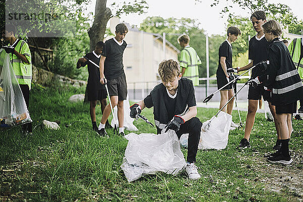 Junge kniet  während er in der Nähe von Freunden Müll in einer Plastiktüte sammelt