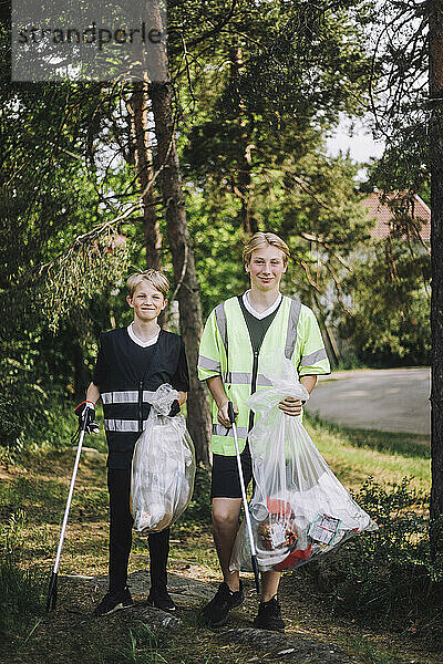 Ganzkörperporträt lächelnder Jungen  die mit Müllsäcken spazieren gehen