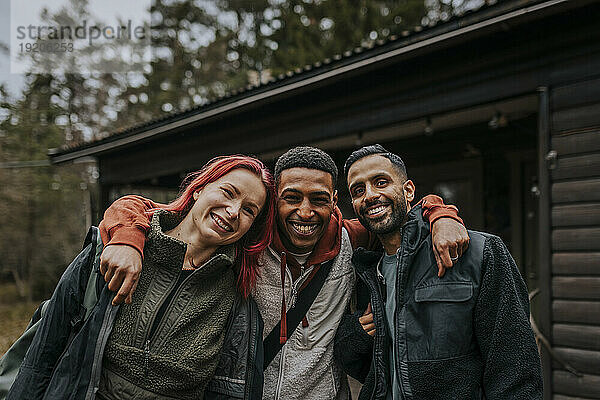 Porträt fröhlicher  gemischtrassiger Freunde  die im Urlaub vor der Hütte stehen