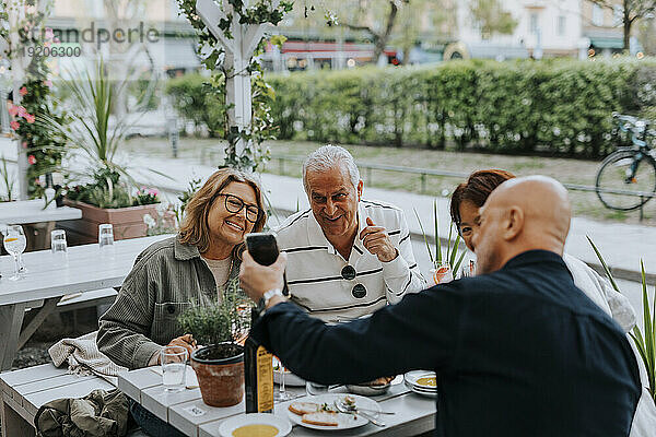 Senior man showing smart phone to male and female friends sitting at restaurant