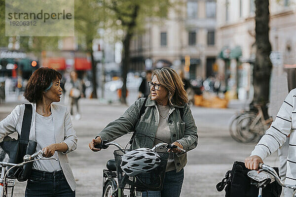 Ältere Freundinnen reden miteinander  während sie Fahrräder fahren
