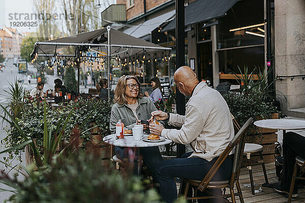 Fröhliche männliche und weibliche ältere Freunde reden miteinander  während sie im Straßencafé essen