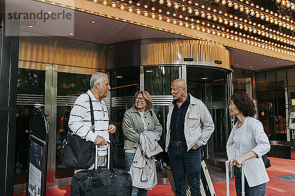 Älterer Mann im Gespräch mit männlichen und weiblichen Freunden  die mit Gepäck vor dem Kino stehen