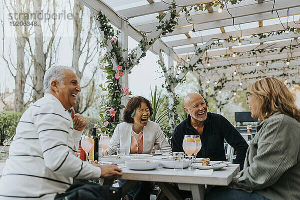Cheerful male and female senior friends laughing while having food at restaurant