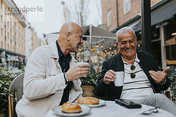 Fröhliche ältere männliche Freunde  die sich beim Kaffeetrinken im Straßencafé amüsieren