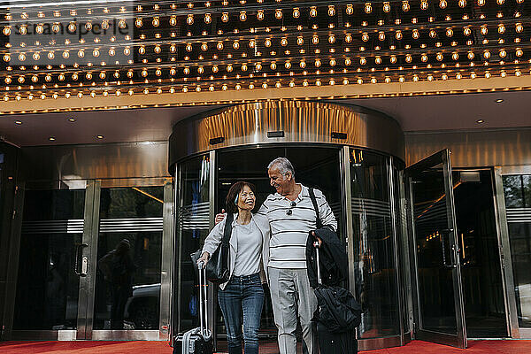 Smiling male and female senior friends walking in front of illuminated movie theater