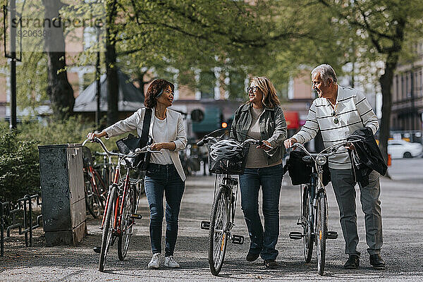 Männliche und weibliche ältere Freunde unterhalten sich  während sie Fahrräder auf dem Fußweg rollen