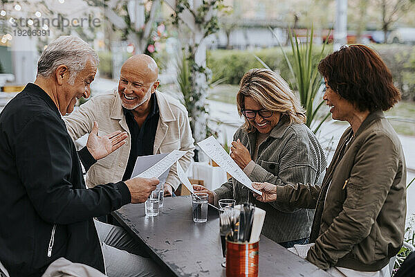 Glückliche männliche und weibliche ältere Freunde genießen es  während sie im Restaurant die Speisekarte lesen
