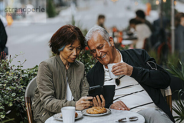 Ältere Frau teilt Smartphone mit älterem Mann  der Kaffeetasse im Straßencafé hält