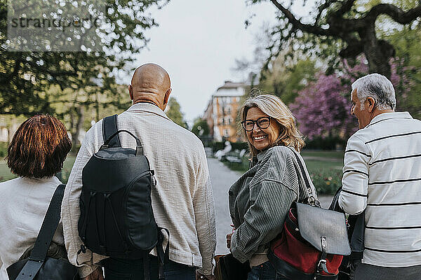 Porträt einer glücklichen älteren Frau  die beim Spaziergang mit Freunden im Park über die Schulter schaut