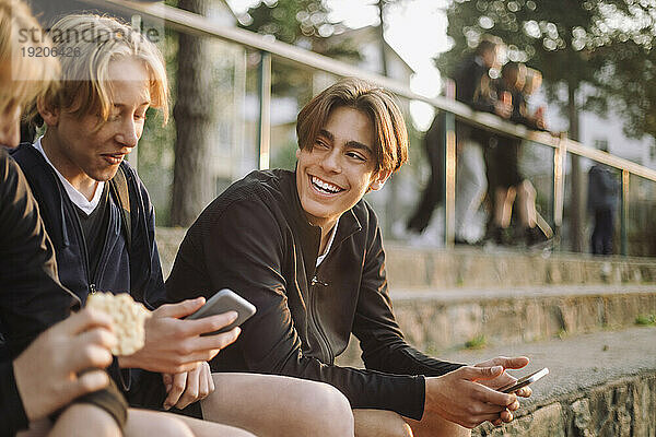 Fröhliche Teenager sitzen mit Smartphones