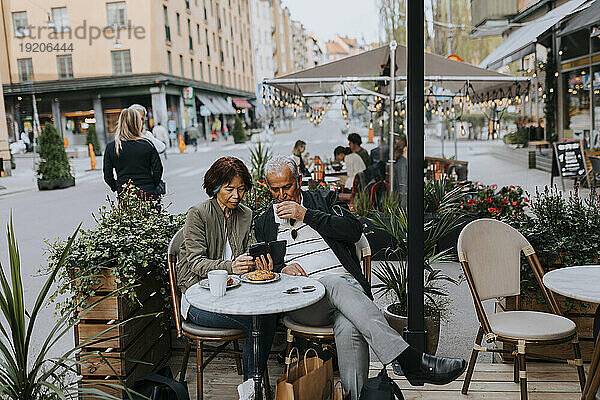 Ältere Frau teilt Smartphone mit älterem männlichen Freund und trinkt Kaffee im Straßencafé