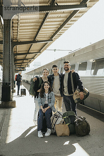 Porträt einer glücklichen Familie mit Gepäck  die zusammen am Bahnhof steht