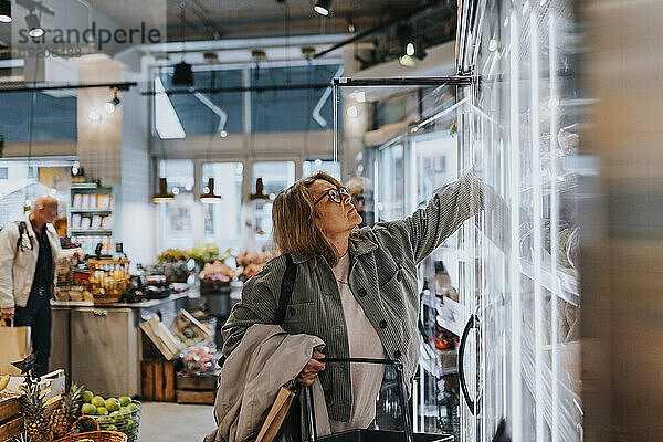 Ältere Frau greift beim Lebensmitteleinkauf im Supermarkt nach dem Produkt