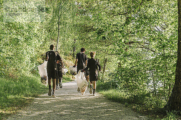 Ganzkörperansicht von hinten: Jungen  die auf einem Fußweg inmitten grüner Pflanzen herumtollen