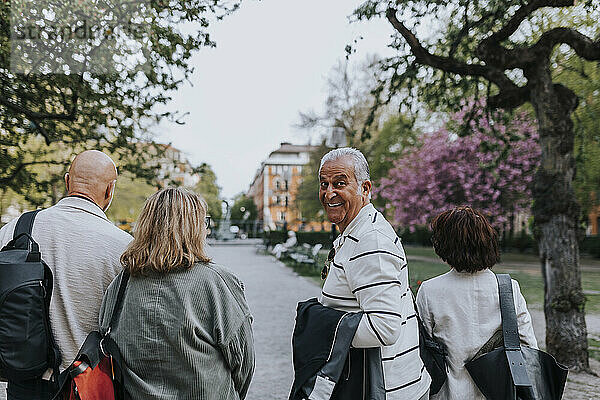 Porträt eines lächelnden älteren Mannes  der beim Spazierengehen mit Freunden im Park über die Schulter schaut