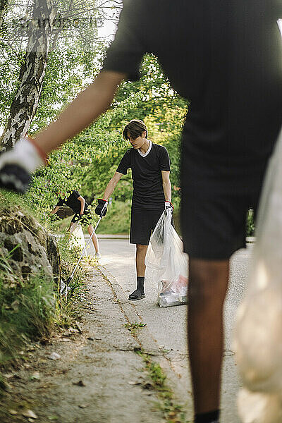 Teenager sammeln unterwegs Plastik von Pflanzen in Müllsäcken