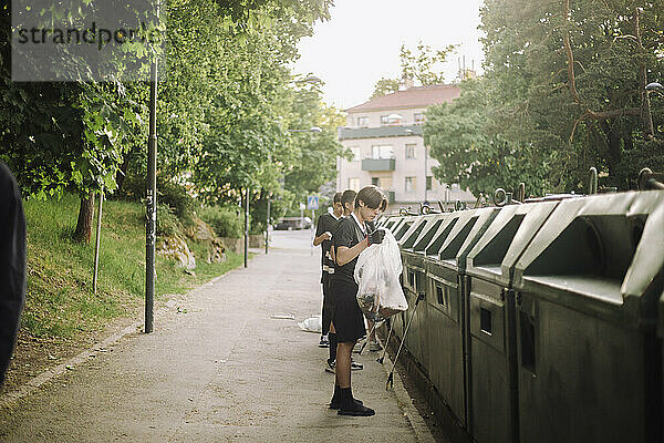 Jungen mit Plastikmüll stehen am Papierkorb