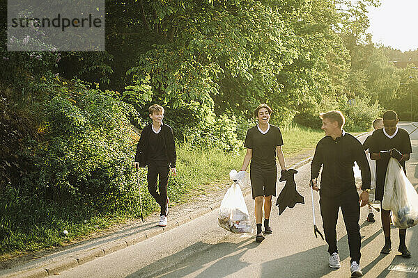 Mann geht mit glücklichen Jungs und Müllsäcken auf der Straße spazieren