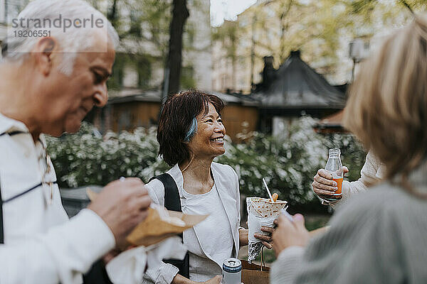 Smiling senior woman enjoying snacks with friends while standing at street