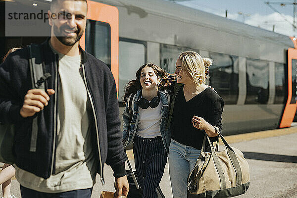 Glückliche Familie  die an einem sonnigen Tag am Bahnhof aus dem Zug aussteigt