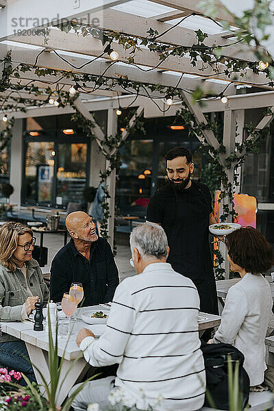 Lächelnder männlicher Kellner  der älteren Kunden im Restaurant Essen serviert