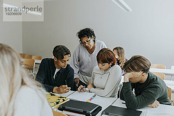 Lehrer steht hinter Schülern  die am Schreibtisch im Klassenzimmer lernen