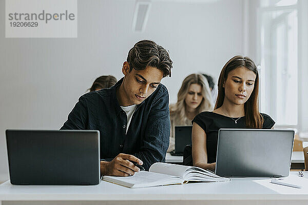 Gemischtrassige männliche und weibliche Teenager studieren am Schreibtisch im Klassenzimmer