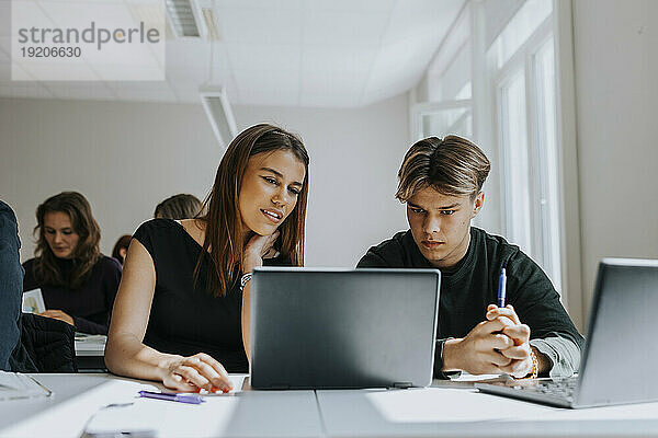 Gemischtrassige männliche und weibliche Studenten teilen sich Laptop am Schreibtisch im Klassenzimmer