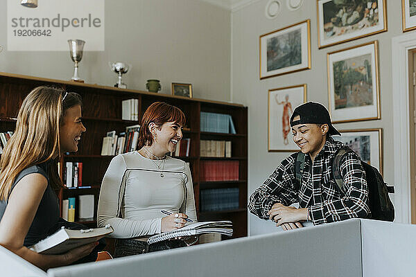 Glückliche männliche und weibliche Studenten reden gegen Bücherregal in der Bibliothek