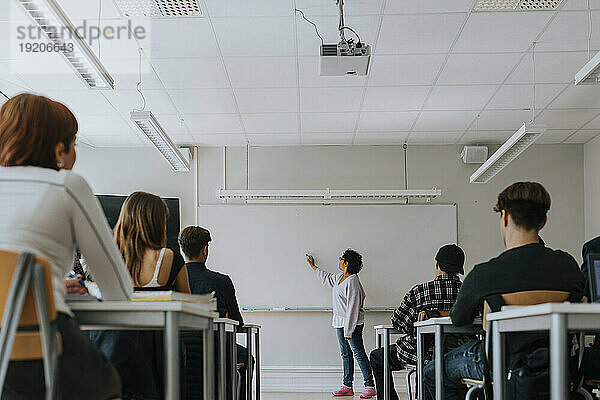 Schüler sitzen am Schreibtisch  während der Lehrer im Klassenzimmer auf dem Whiteboard schreibt