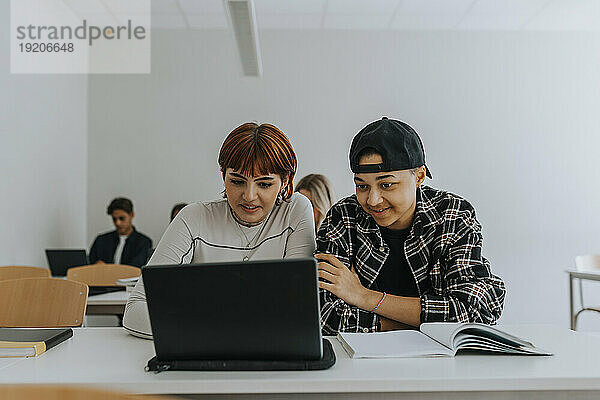 Männer und Frauen nutzen gemeinsam Laptop am Schreibtisch im Klassenzimmer