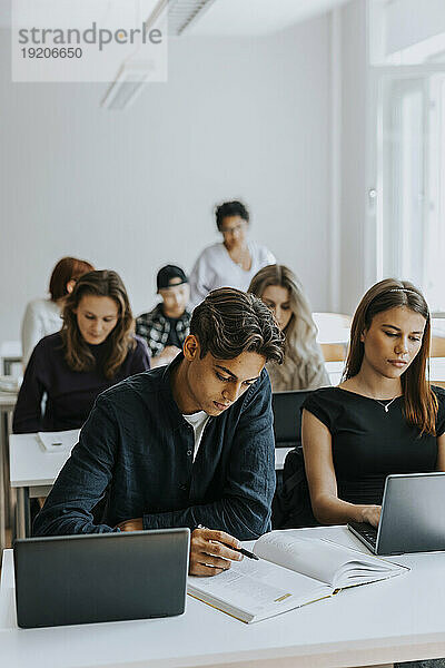 Männliche und weibliche Studenten sitzen am Schreibtisch  während sie im Klassenzimmer lernen