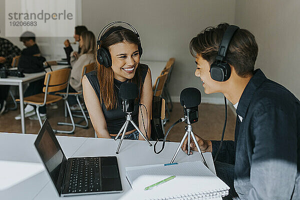 Lächelnde Studentinnen und Studenten schauen sich beim Podcasting im Klassenzimmer an