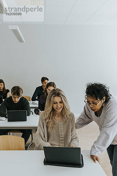 Lehrer unterstützt junge Frau mit Laptop gegen Schüler im Klassenzimmer